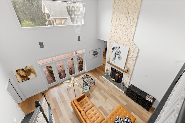 living room with an inviting chandelier, hardwood / wood-style floors, a towering ceiling, and a fireplace