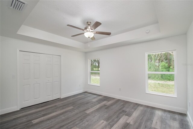 unfurnished bedroom featuring ceiling fan, multiple windows, and a tray ceiling