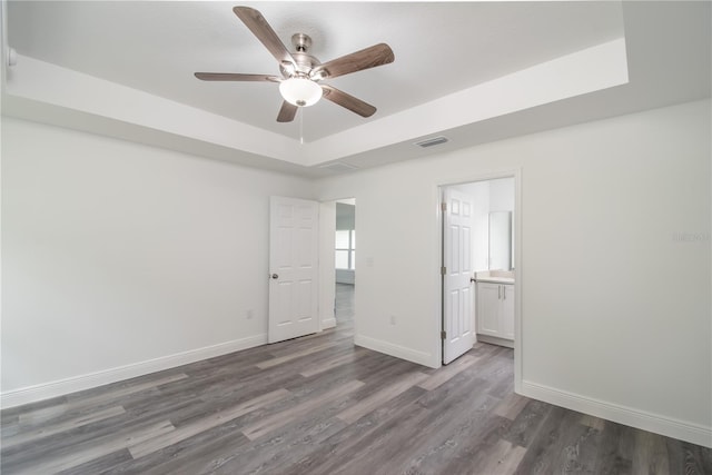 unfurnished bedroom featuring ceiling fan, dark wood-type flooring, ensuite bathroom, and a raised ceiling