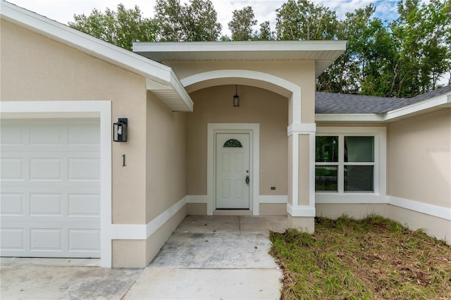 entrance to property featuring roof with shingles, an attached garage, and stucco siding