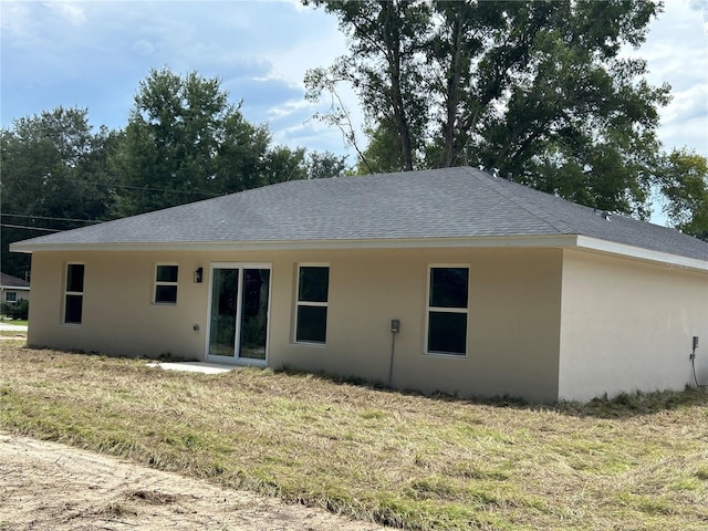 rear view of house featuring stucco siding, roof with shingles, and a lawn
