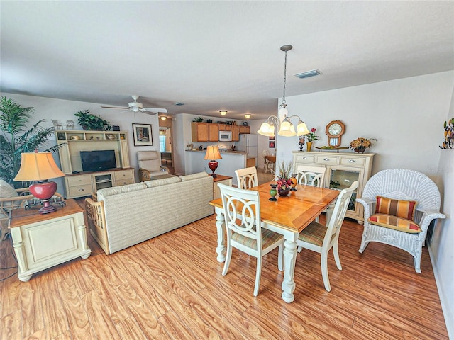 dining room featuring ceiling fan with notable chandelier and light hardwood / wood-style flooring