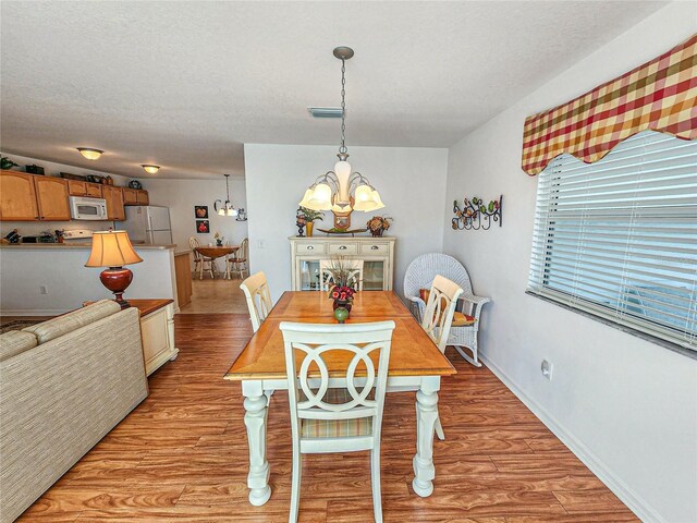 dining area with light hardwood / wood-style floors, an inviting chandelier, and a textured ceiling