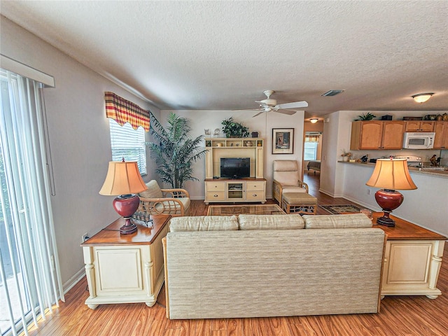 living room with light hardwood / wood-style floors, a textured ceiling, and ceiling fan