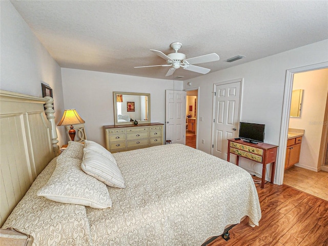 bedroom featuring light hardwood / wood-style flooring, ensuite bathroom, a textured ceiling, and ceiling fan