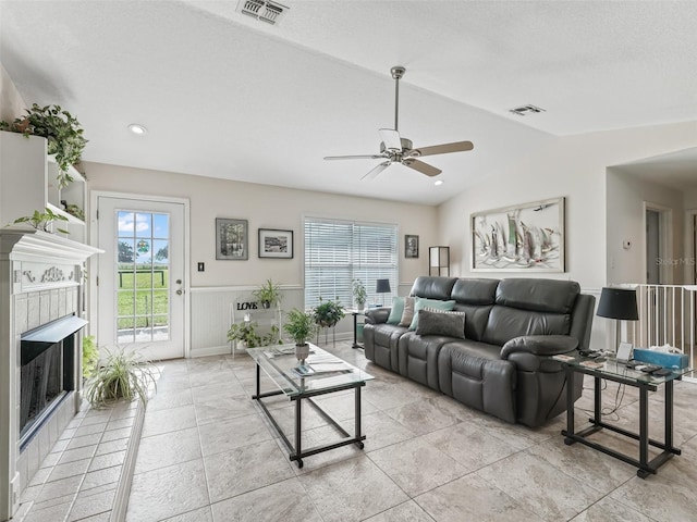 living room with ceiling fan, a tile fireplace, a textured ceiling, and vaulted ceiling