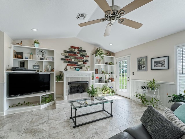 living room featuring a wealth of natural light, ceiling fan, a tile fireplace, and vaulted ceiling