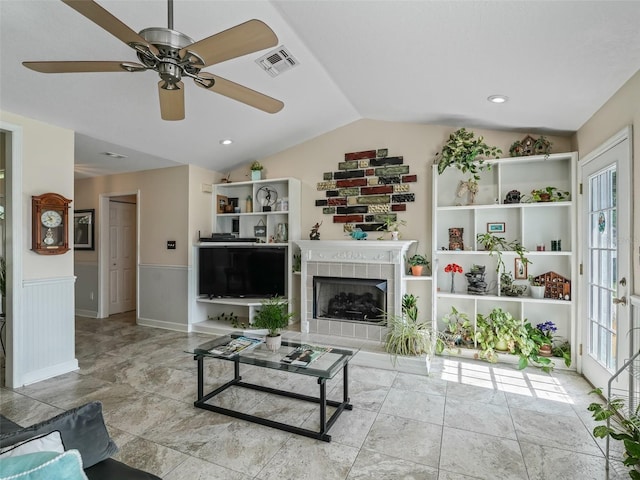 living room with built in shelves, lofted ceiling, a tile fireplace, and ceiling fan