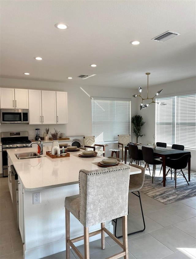 kitchen featuring light tile patterned flooring, white cabinetry, stainless steel appliances, pendant lighting, and an island with sink