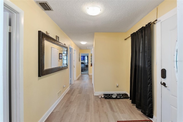 corridor with a textured ceiling and light hardwood / wood-style floors