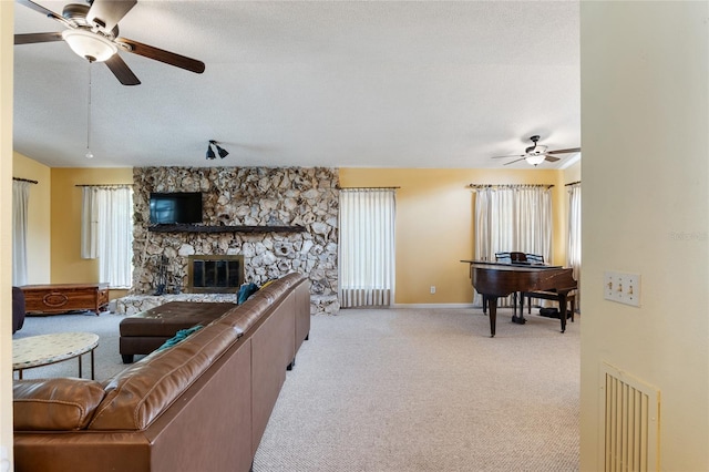 living room with a textured ceiling, ceiling fan, a stone fireplace, and light colored carpet