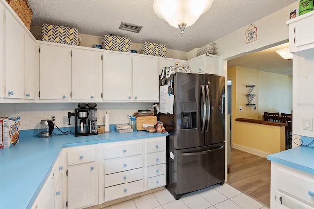 kitchen featuring white cabinetry, light hardwood / wood-style floors, black refrigerator with ice dispenser, and a textured ceiling