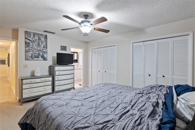 bedroom featuring ceiling fan, multiple closets, light colored carpet, and a textured ceiling