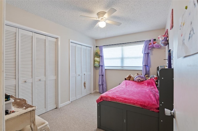 carpeted bedroom with a textured ceiling, ceiling fan, and multiple closets