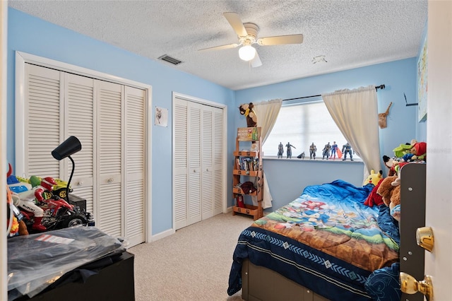 carpeted bedroom with a textured ceiling, ceiling fan, and multiple closets