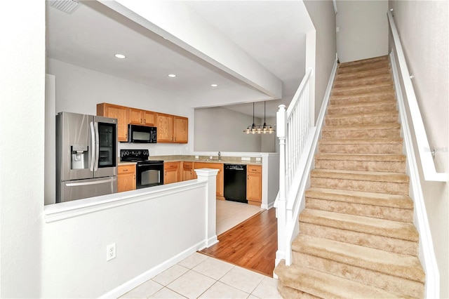 kitchen featuring black appliances, hanging light fixtures, sink, light hardwood / wood-style floors, and kitchen peninsula