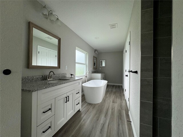 bathroom with a textured ceiling, a tub, vanity, and wood-type flooring