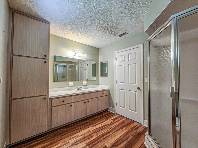 bathroom with a shower with shower door, vanity, a textured ceiling, and wood-type flooring