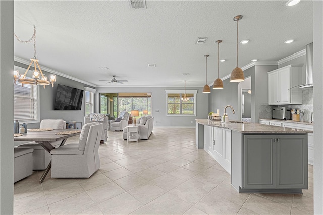 kitchen featuring light stone countertops, ceiling fan with notable chandelier, a kitchen island with sink, hanging light fixtures, and white cabinetry