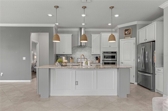 kitchen with wall chimney exhaust hood, a center island with sink, pendant lighting, stainless steel appliances, and white cabinets