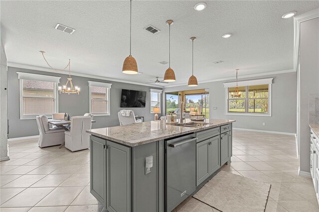 kitchen with ceiling fan with notable chandelier, ornamental molding, light stone counters, an island with sink, and sink