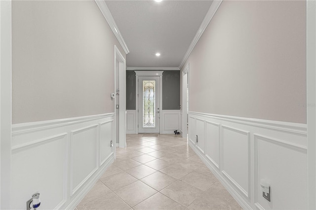 entryway with light tile patterned floors, a decorative wall, crown molding, and a wainscoted wall