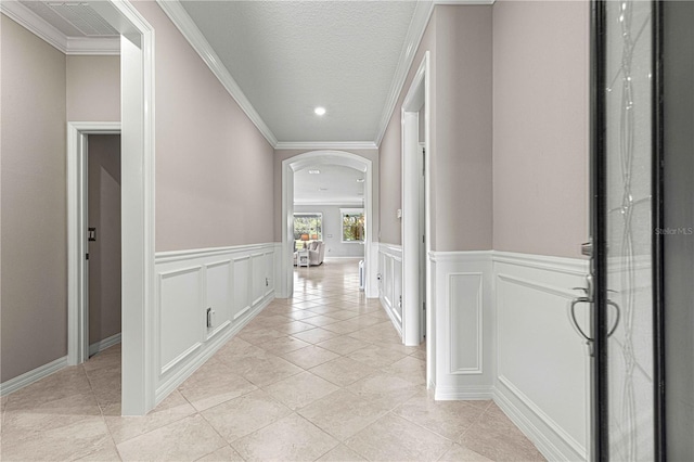 hall featuring crown molding, a decorative wall, light tile patterned flooring, and arched walkways
