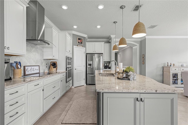 kitchen with visible vents, an island with sink, stainless steel appliances, wall chimney exhaust hood, and a sink