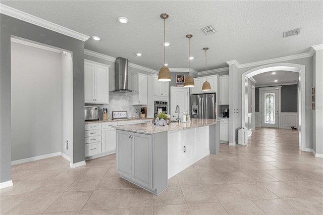 kitchen with decorative light fixtures, light stone countertops, stainless steel appliances, wall chimney exhaust hood, and a center island with sink