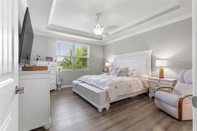 bedroom featuring a textured ceiling, a raised ceiling, hardwood / wood-style floors, ornamental molding, and ceiling fan