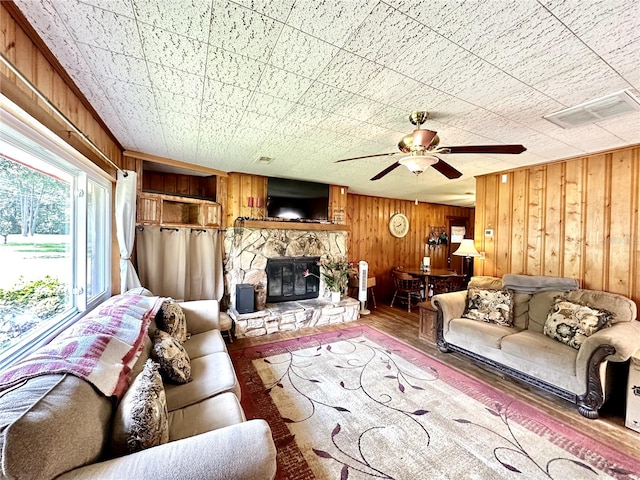 living room featuring wooden walls, ceiling fan, hardwood / wood-style flooring, and a stone fireplace