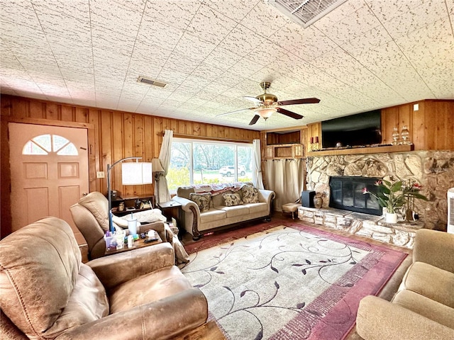 living room featuring a stone fireplace, wood walls, ceiling fan, and hardwood / wood-style flooring