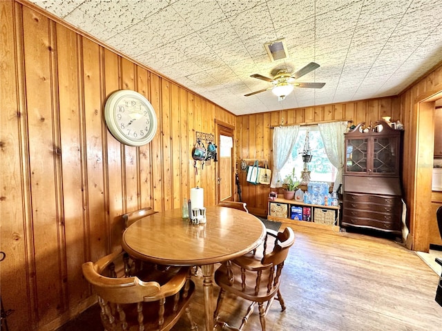 dining space featuring wood-type flooring, wooden walls, and ceiling fan