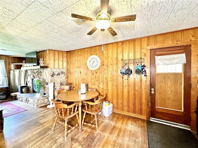 dining area with a wood stove, wood walls, ceiling fan, and hardwood / wood-style floors