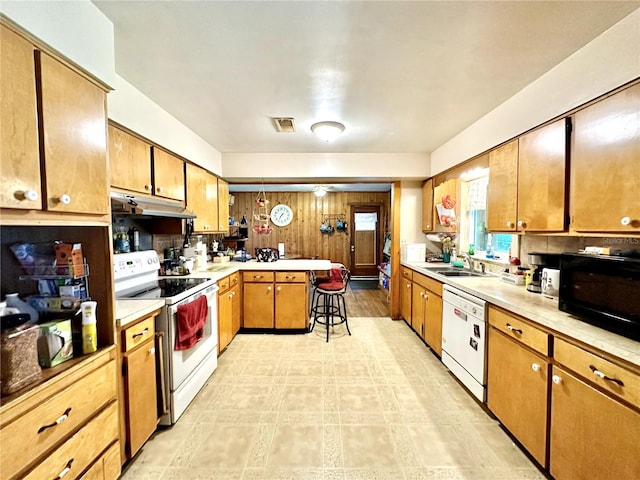 kitchen with kitchen peninsula, sink, white appliances, tasteful backsplash, and a kitchen breakfast bar