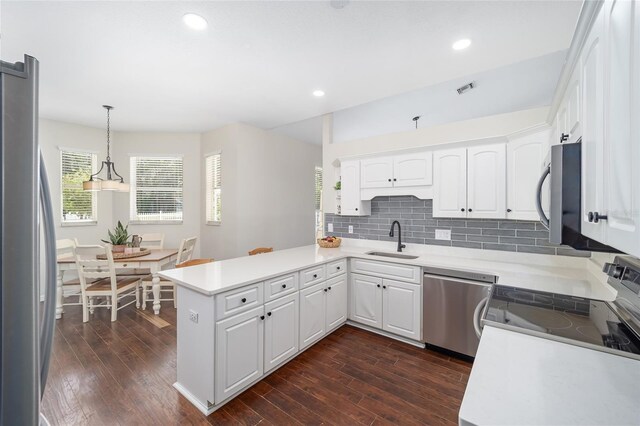 kitchen featuring kitchen peninsula, stainless steel appliances, pendant lighting, white cabinets, and sink