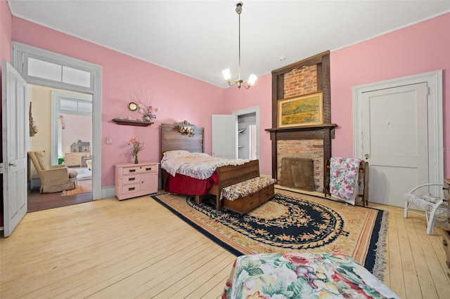 bedroom featuring a fireplace, a chandelier, crown molding, brick wall, and light hardwood / wood-style flooring