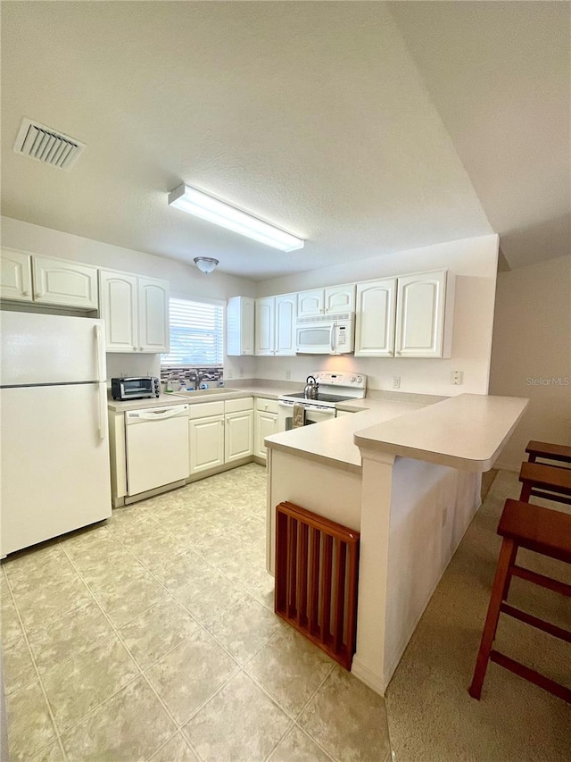 kitchen with white cabinets, white appliances, a breakfast bar, kitchen peninsula, and light tile patterned floors