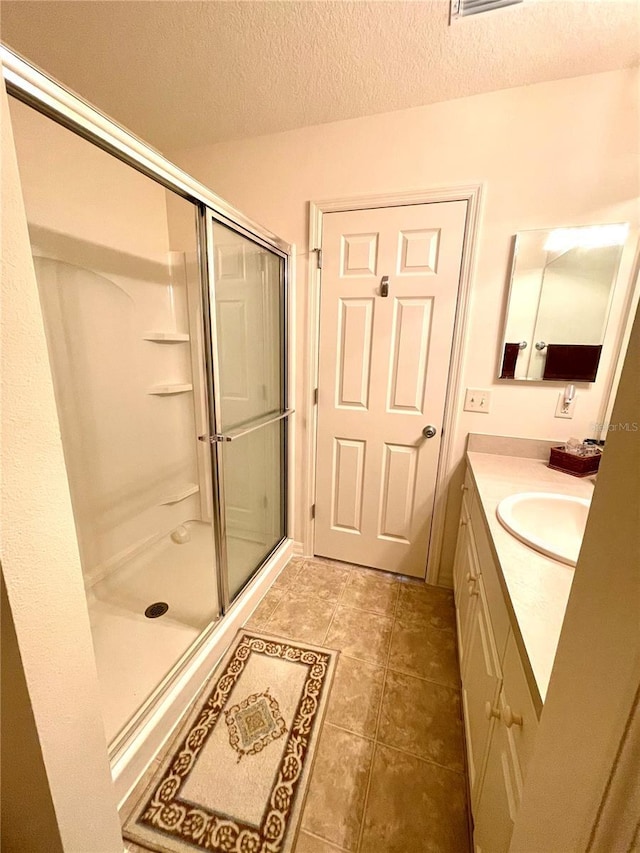 full bath with a textured ceiling, tile patterned flooring, a shower stall, and vanity