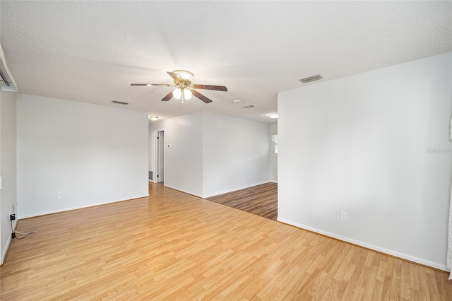 empty room featuring light wood-type flooring, ceiling fan, visible vents, and a textured ceiling