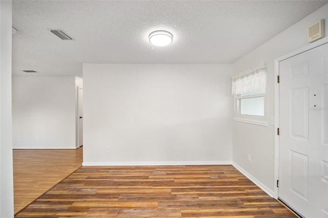 unfurnished room featuring baseboards, a textured ceiling, visible vents, and wood finished floors