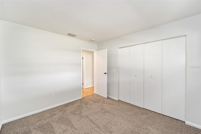 unfurnished bedroom featuring a closet, visible vents, light carpet, a textured ceiling, and baseboards