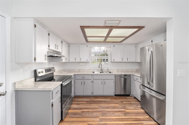 kitchen with stainless steel appliances, light countertops, a sink, wood finished floors, and under cabinet range hood