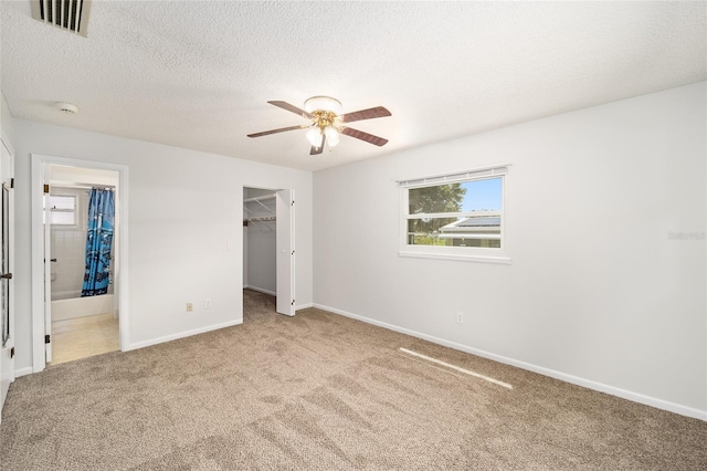 unfurnished bedroom with ensuite bathroom, carpet flooring, a walk in closet, a closet, and ceiling fan