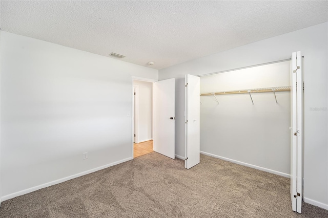 unfurnished bedroom featuring a textured ceiling, light colored carpet, visible vents, baseboards, and a closet