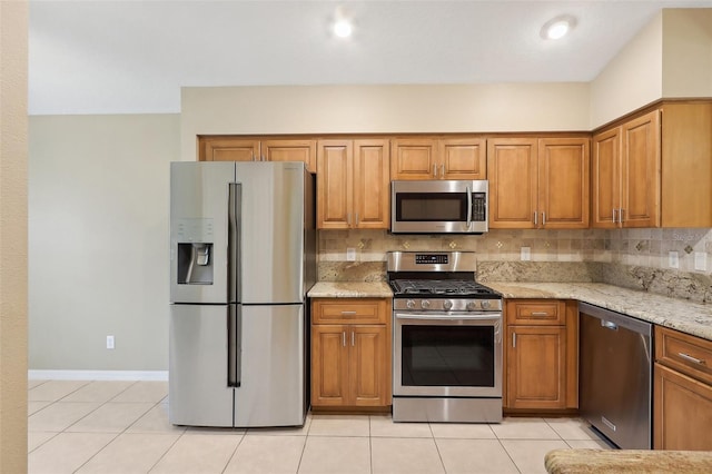 kitchen with appliances with stainless steel finishes, light tile patterned flooring, decorative backsplash, and light stone countertops