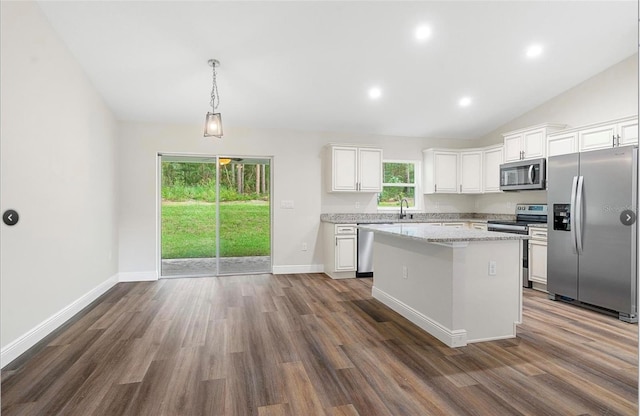 kitchen with a kitchen island, white cabinetry, hanging light fixtures, light stone countertops, and stainless steel appliances