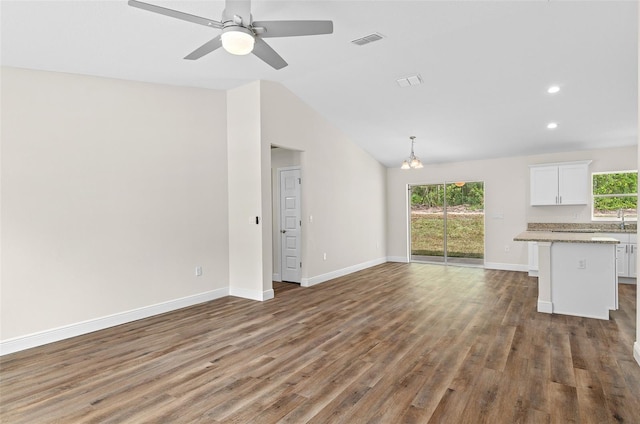 unfurnished living room featuring ceiling fan with notable chandelier, dark wood-type flooring, a healthy amount of sunlight, and vaulted ceiling