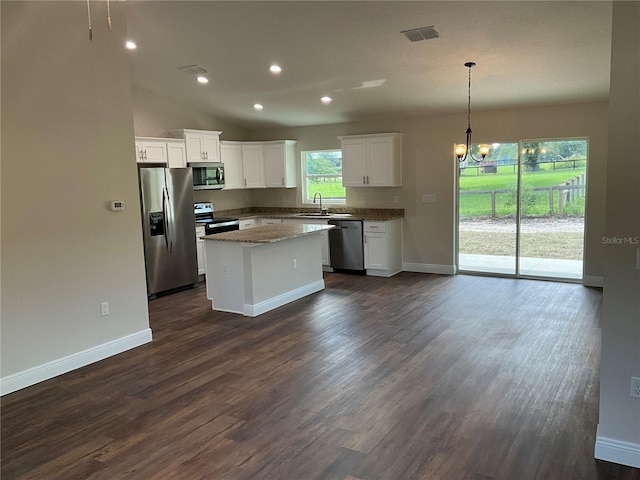 kitchen featuring appliances with stainless steel finishes, hanging light fixtures, light stone countertops, a kitchen island, and white cabinets