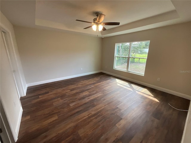 empty room featuring dark wood-type flooring, a tray ceiling, and ceiling fan